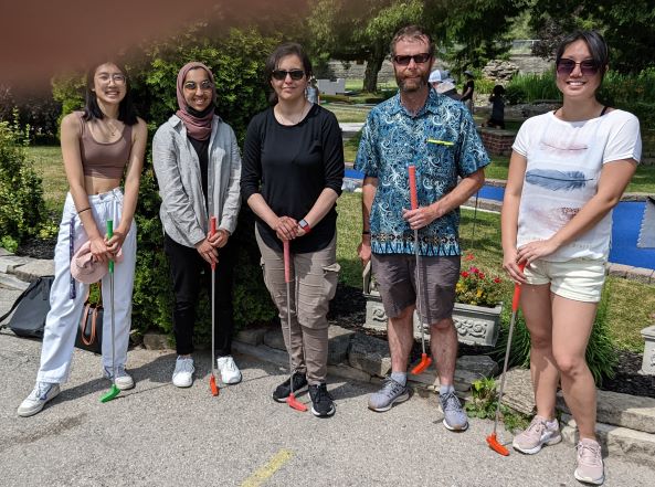 Sinclar lab holding mini-golf clubs. There's a finger in the corner of the frame
